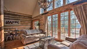 A log cabin interior with a wooden dining table, two sofas, a chandelier, and large windows. - ‘Snow Pine Retreat’ - Remote Crescent Log Cabin! (Crescent)