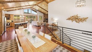 Un intérieur spacieux avec un plafond en bois, un coin repas, un escalier et une vue sur l’extérieur.