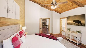 Une chambre à coucher avec un lit, un plafond en bois, une cheminée en pierre, un tableau représentant un ours et une console.