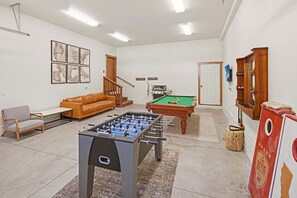 Una habitación con mesa de futbolín, mesa de billar, sofá, silla y escalera de madera.