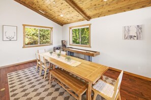 En matplats med ett träbord och träbänkar, stora fönster med utsikt över grönområden och ett tak med synliga träbjälkar.