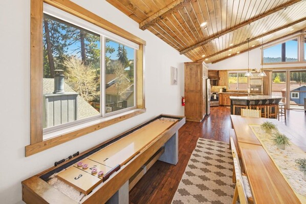 Una habitación con mesa de juego de hojalata, suelo de madera, un ventanal y vistas al exterior.