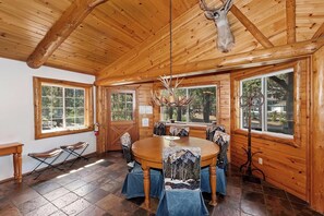 L’intérieur d’un chalet en bois, avec une table à manger ronde, des chaises, un lustre et de grandes fenêtres.