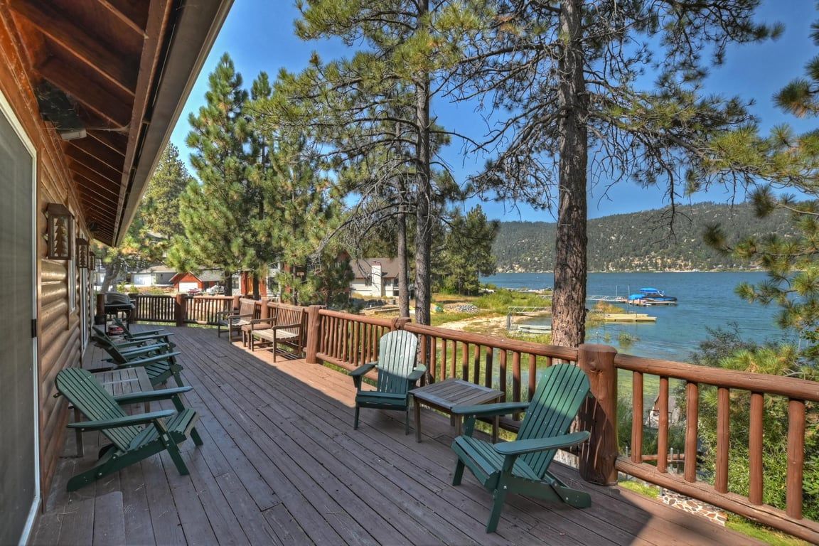 Terraza de madera con mobiliario exterior, con vistas a un lago con barcos y un muelle.