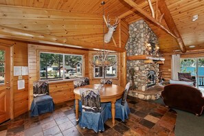 L’intérieur d’une cabane en rondins, avec une cheminée en pierre, une table à manger en bois et des chaises.