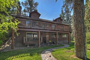 Une cabane en rondins à deux étages, dotée d’un balcon, d’un chemin en pierre et d’un grand arbre au premier plan.