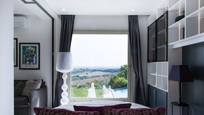 Ein Schlafzimmer mit großem Fenster, einem Bett mit gemusterten Kissen, einer Chandelüster und einem Gemälde an der Wand.