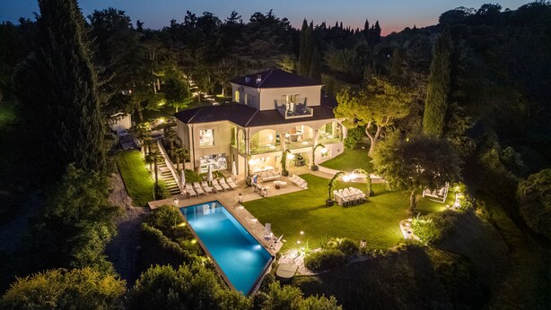 Ein großes Haus mit Swimmingpool, Sitzgelegenheiten im Freien und einem gut beleuchteten Garten bei Nacht.