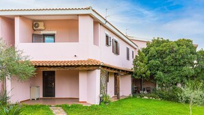 Une villa rose avec un toit en tuiles, un patio couvert et un jardin bien entretenu.