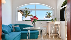 A room with a teal sofa, a small round table with a vase of flowers, a white chair, and a large arched window with a view of palm trees. - Villa Alex with WiFi and Pool (Puerto del Carmen)