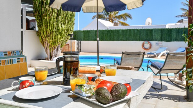 A table with breakfast items, a coffee pot, and a pool in the background. - Villa Alex with WiFi and Pool (Puerto del Carmen)