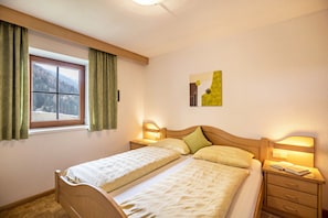 A double bed with a wooden headboard, two bedside tables with lamps, a window with curtains, and a wall-mounted artwork.