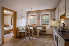 A compact kitchen with a dining area, wooden furniture, and a view through the window.