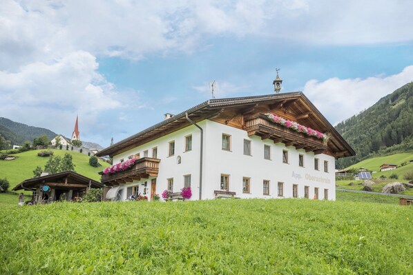 A white building with a sloped roof, wooden balconies, and a sign reading 'App. Oberachrin.'