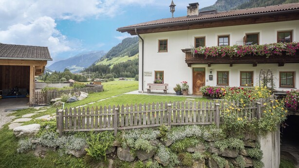 Un chalet traditionnel avec des fondations en pierre, un balcon en bois orné de fleurs et une vue sur les montagnes.