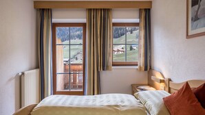 Une chambre à coucher avec un lit, une table de chevet, une fenêtre avec des rideaux et une vue sur un paysage montagneux.
