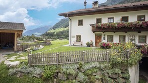 A white building with a wooden balcony, a stone wall, and a wooden fence. - Apartment “Bärental” in Beautiful Scenery with Mountain View, Wi-Fi & Garden (St.Jakob im Ahrntal)
