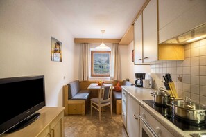 Une cuisine compacte dotée d’une cuisinière intégrée, d’un coin repas avec un banc et d’un téléviseur posé sur un meuble.