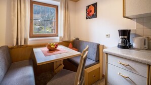 A compact kitchen with a dining area, a window with curtains, a coffee maker, and a bowl of fruit on the table. - Apartment “Bärental” in Beautiful Scenery with Mountain View, Wi-Fi & Garden (St.Jakob im Ahrntal)