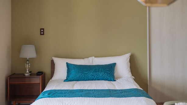 Una habitación de hotel con una cama, una mesita de noche con lámpara y un interruptor de pared.