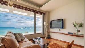 A modern hotel room with a leather sofa, a wooden table, a TV, and a view of the ocean. - HOTEL Churabeach (Motobu)