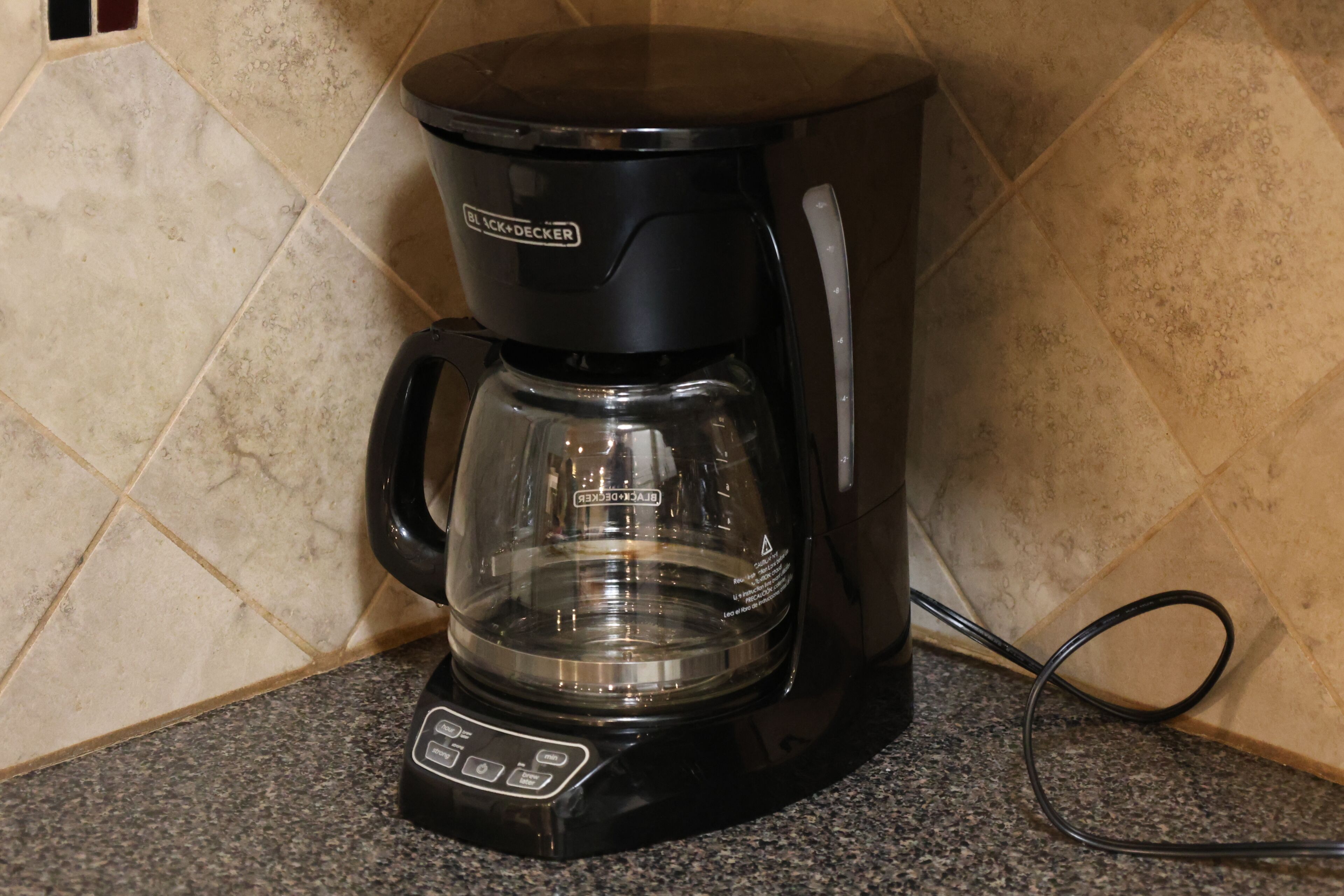 A black coffee maker with a glass carafe on a granite countertop.