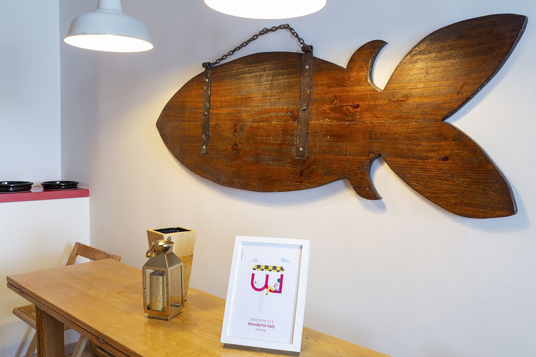 Une décoration murale représentant un poisson en bois, une petite table avec une lanterne et un panneau d’accueil encadré.