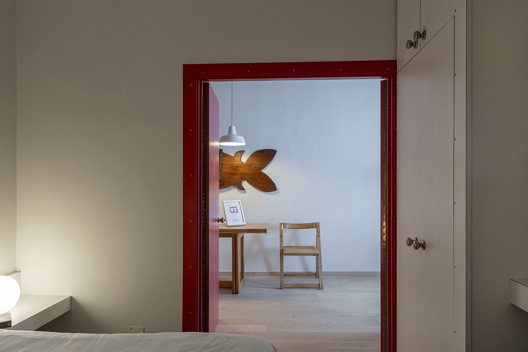 Habitación de hotel con un marco de puerta rojo que da a una pequeña zona de estar con una mesa, una silla y un adorno en la pared.