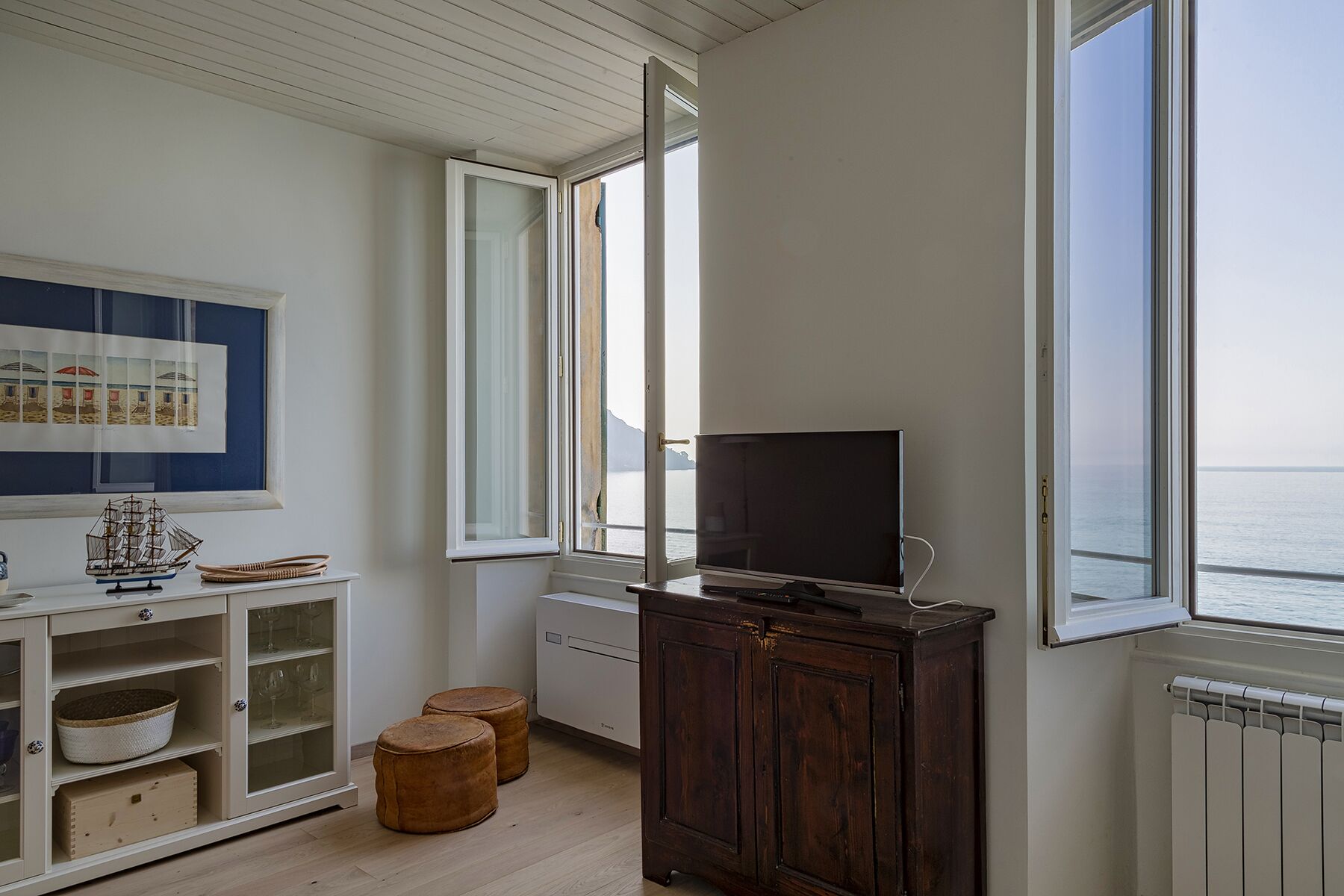 Une pièce avec un meuble en bois, une télévision et une fenêtre donnant sur la mer.