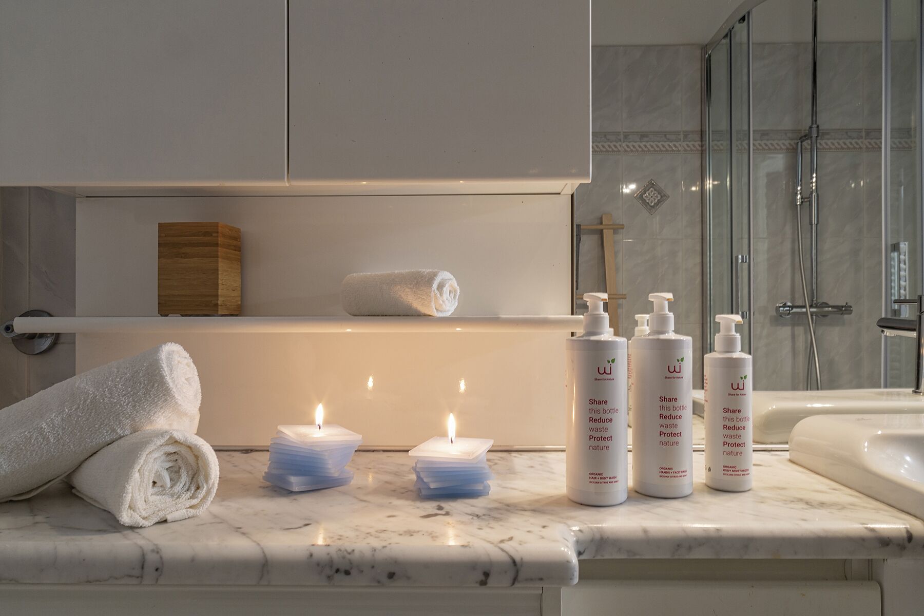 A bathroom with a marble countertop, a towel, candles, and organic body wash bottles.