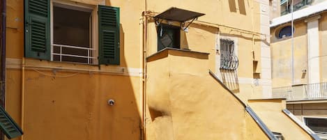 Un bâtiment jaune avec des volets verts, une petite fenêtre et un auvent en métal.