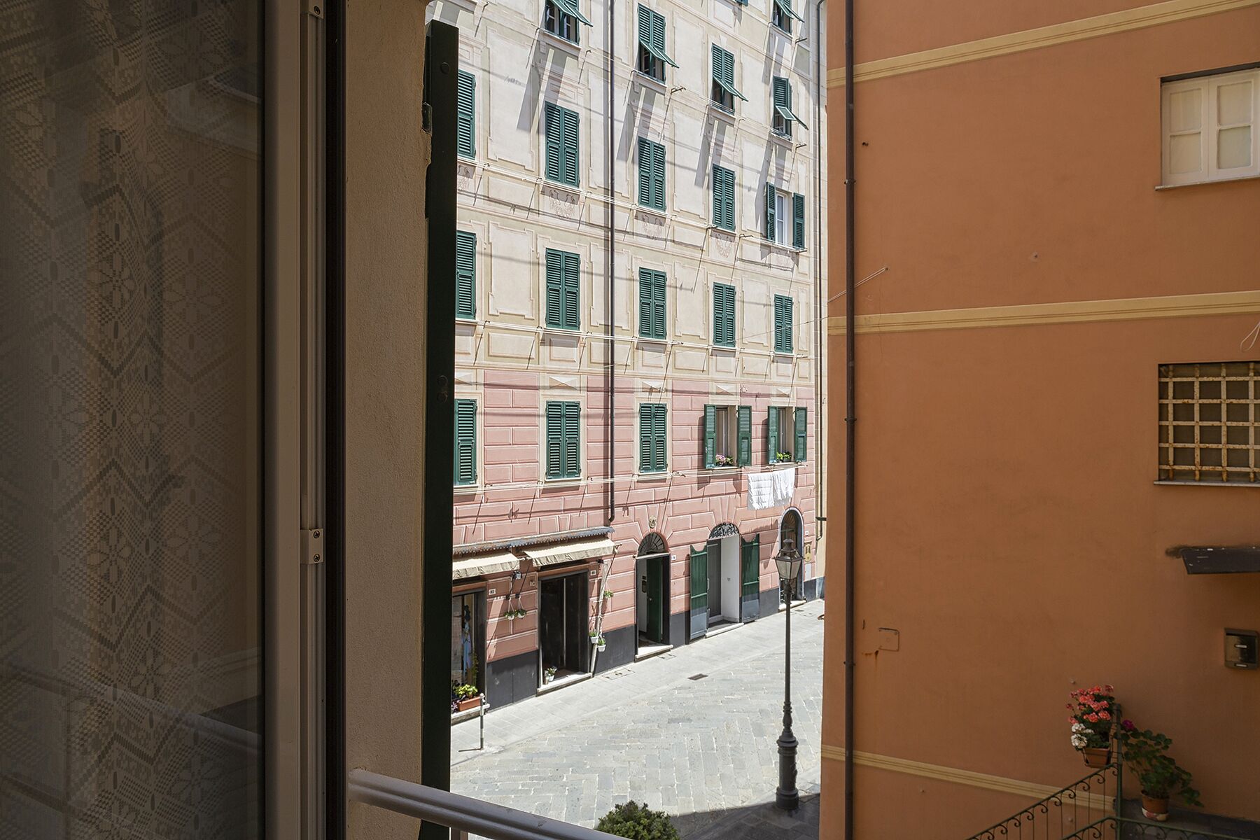 Une vue depuis un balcon donnant sur une rue bordée d’immeubles aux volets verts, avec un ciel dégagé.