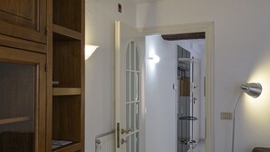 En gang med et træskab, en hvid dør med glasruder, en radiator og en vægmonteret lampe.