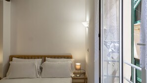 Et soveværelse med en seng, et natbord med en lampe og udsigt gennem et vindue med gardin.