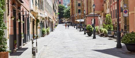 A paved street lined with buildings, outdoor seating, and potted plants.
