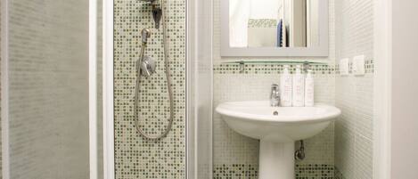 A bathroom with a glass-enclosed shower, a pedestal sink, and a mirror above the sink.