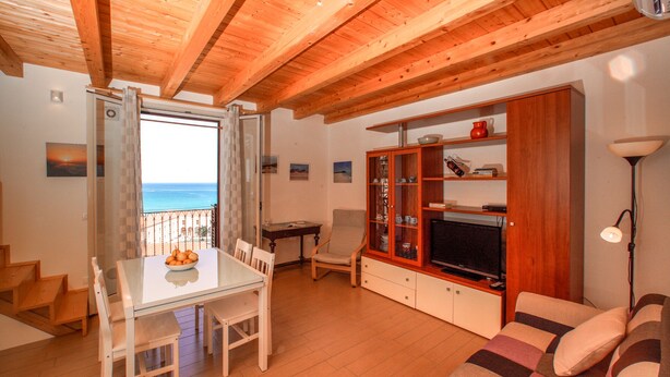 Ein gemütliches Wohnzimmer mit Holzboden, einem Essbereich mit Tisch und Stühlen, einer Couch und einer TV-Kommode.