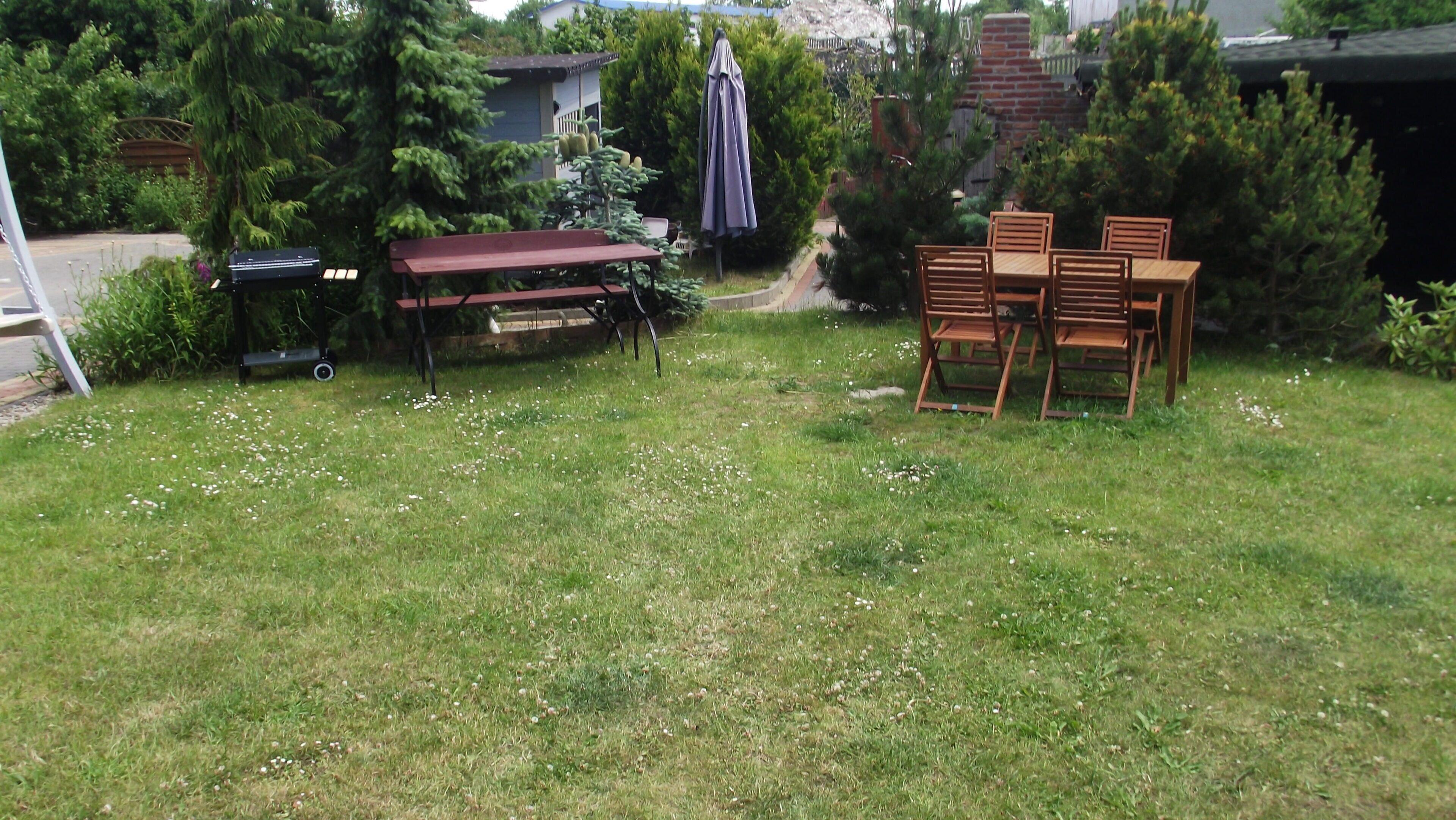 A backyard with a wooden table and chairs, a bench, and a covered umbrella.