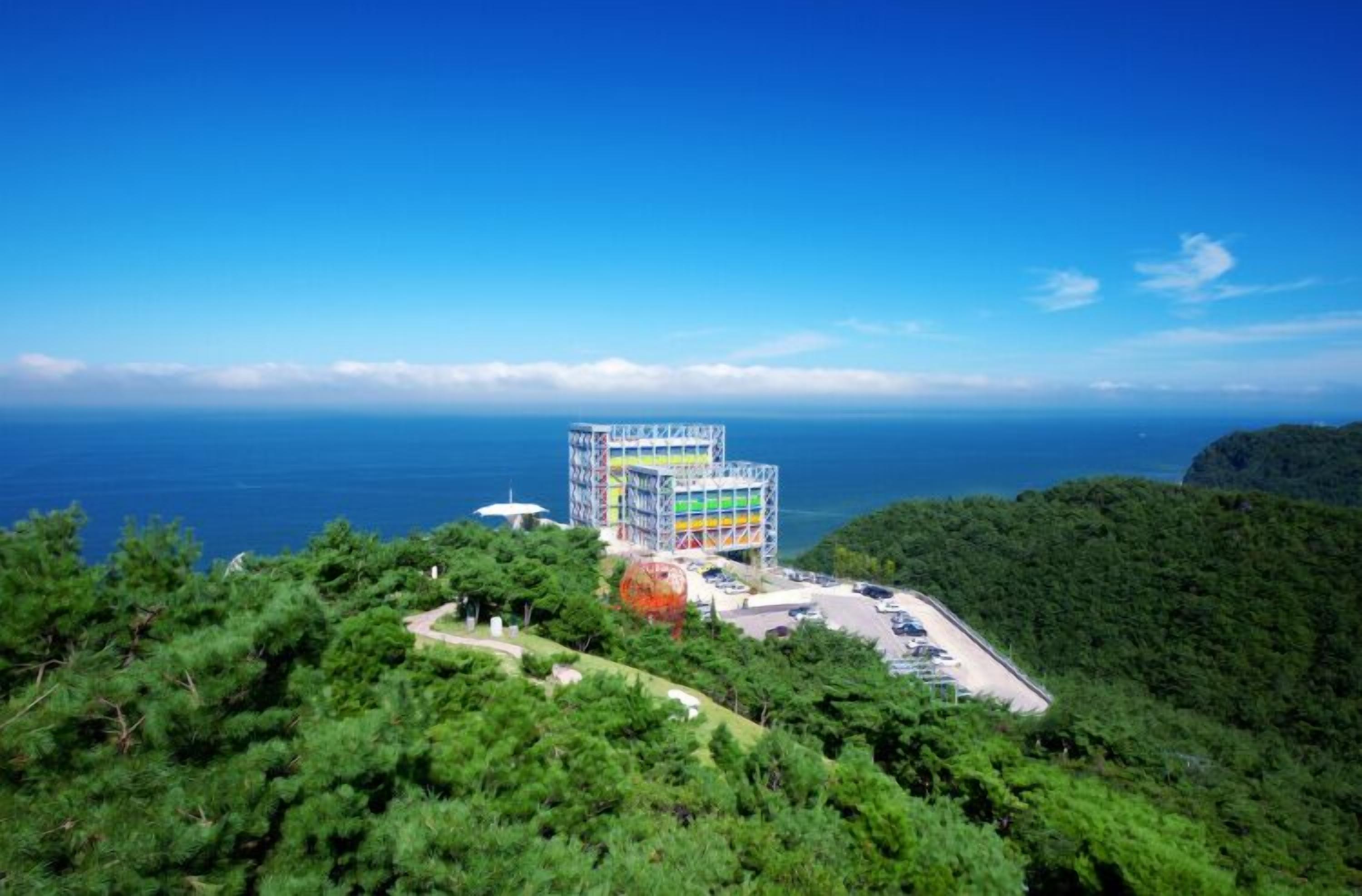 A multi-story building with a unique architectural design, surrounded by lush greenery and overlooking a body of water.