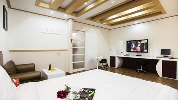 Habitación de hotel moderna con una cama grande, un escritorio con computadora, televisor y armario.