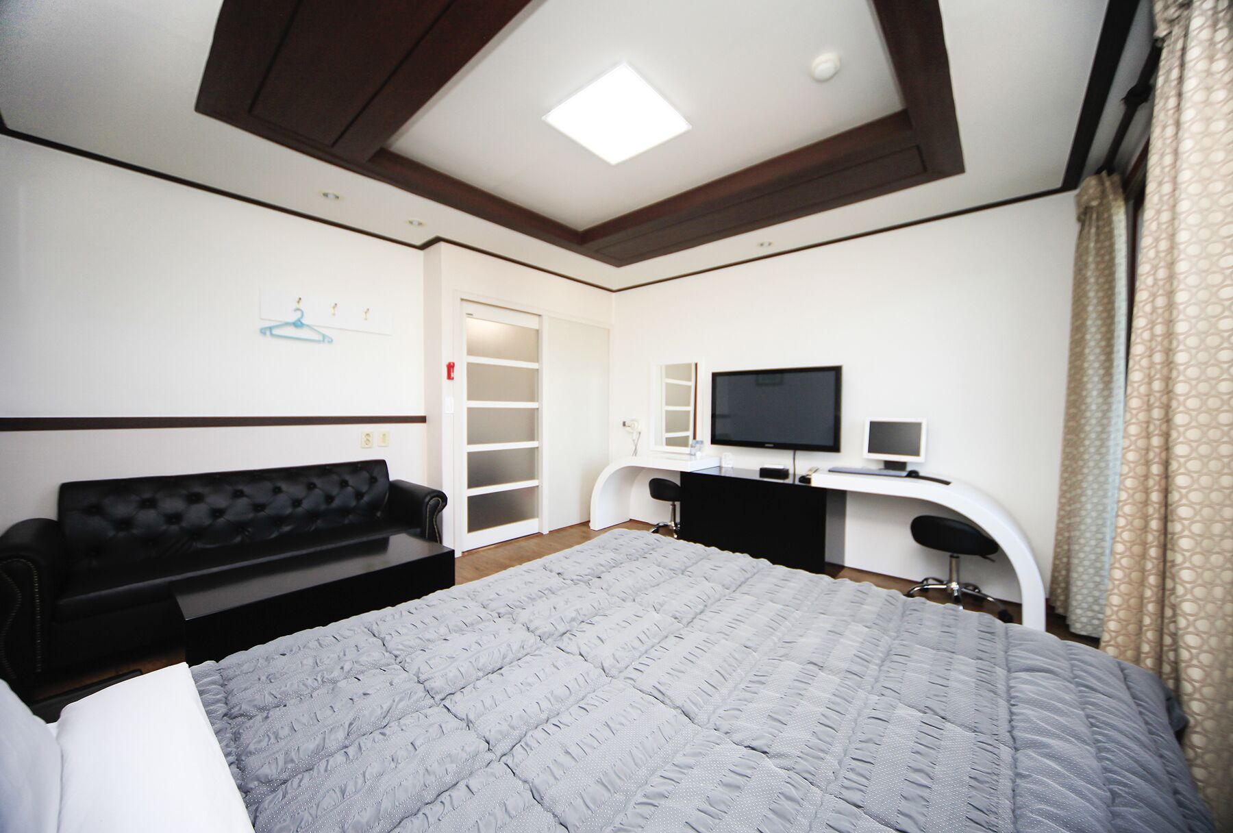 A bedroom with a bed, a desk with a TV, a wardrobe, and a sofa.