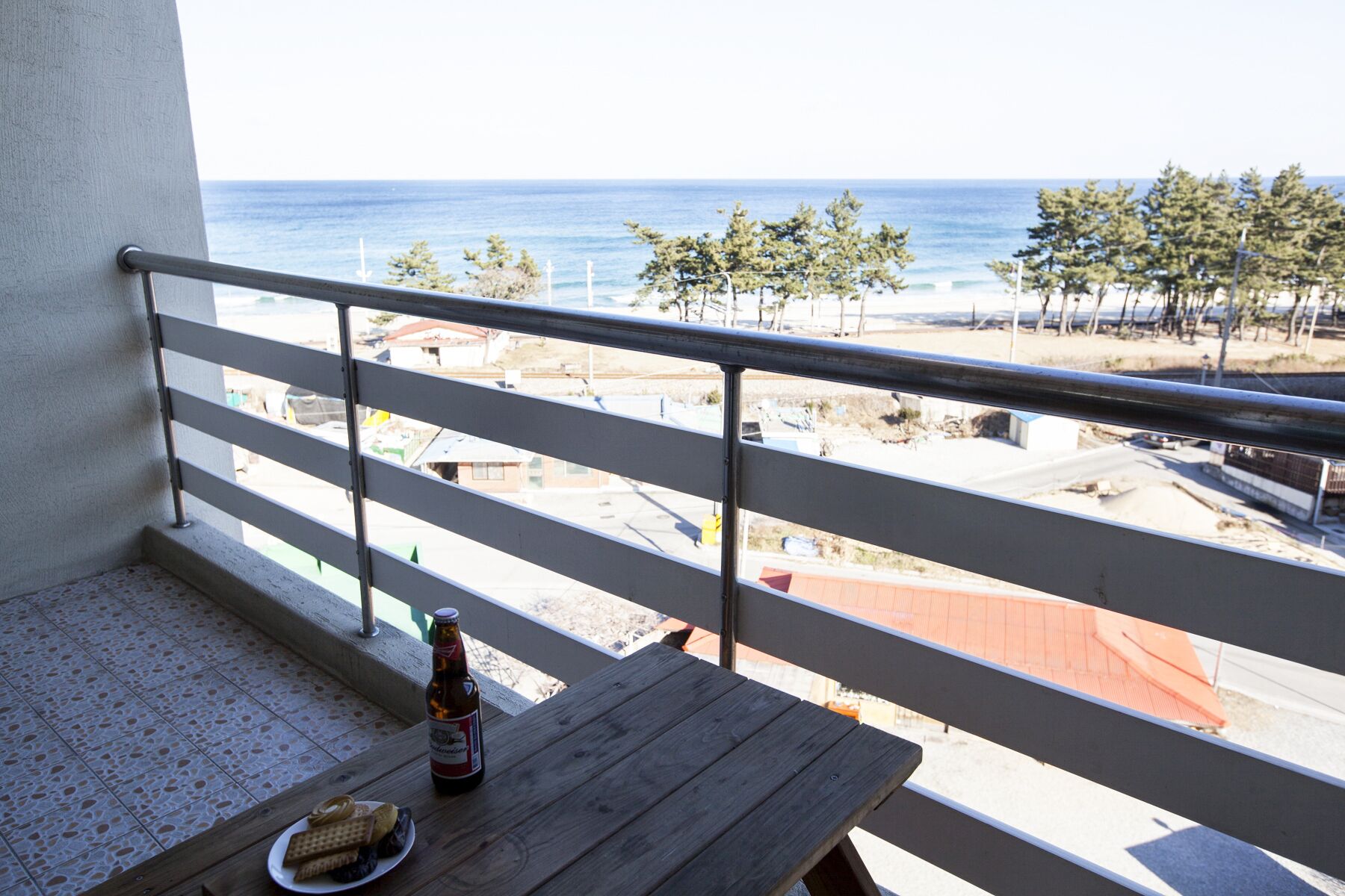 Un balcon avec vue sur la mer, une bouteille de bière et des en-cas sur une table.