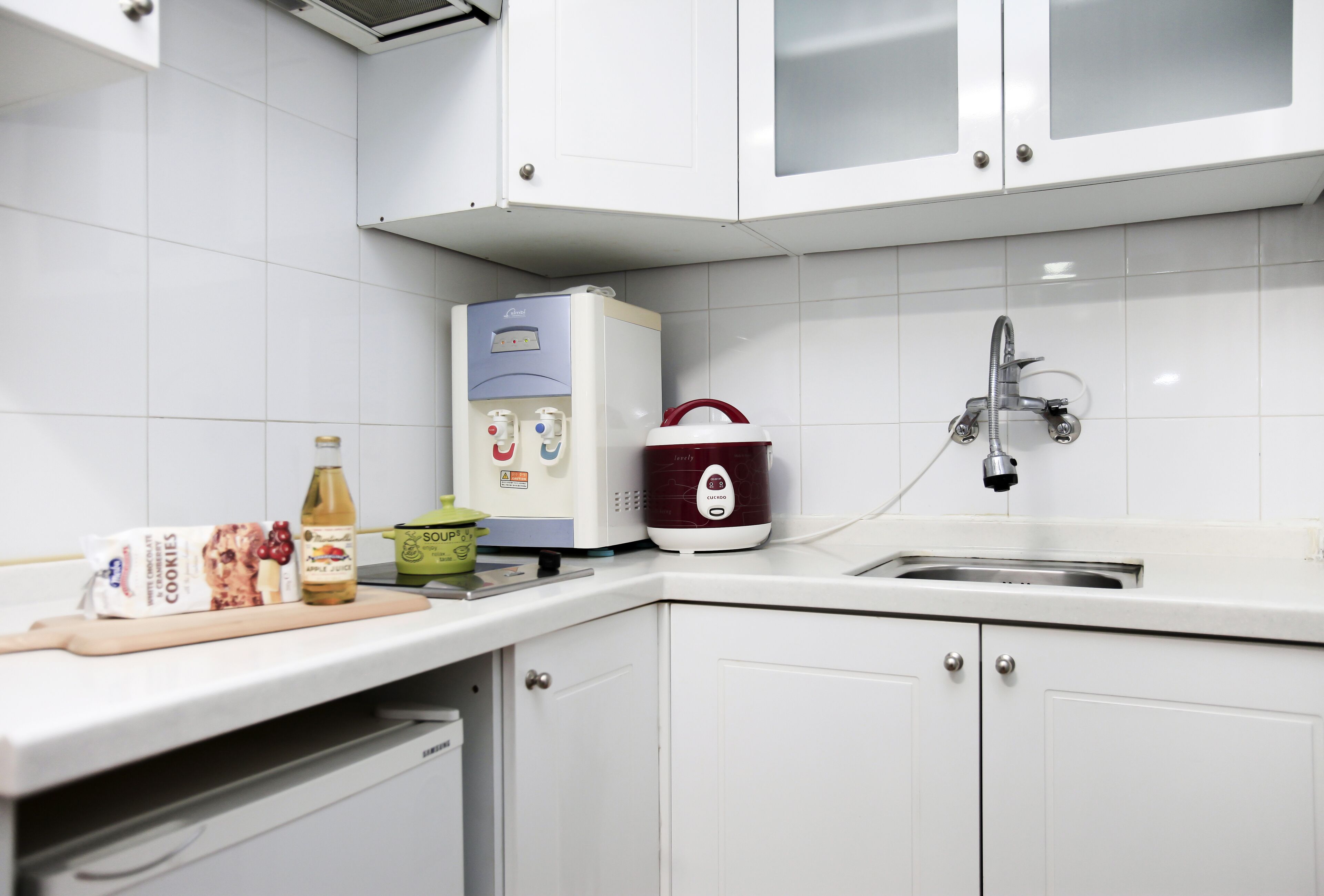 A kitchen with white cabinets, a built-in microwave, a coffee maker, a kettle, and a sink.
