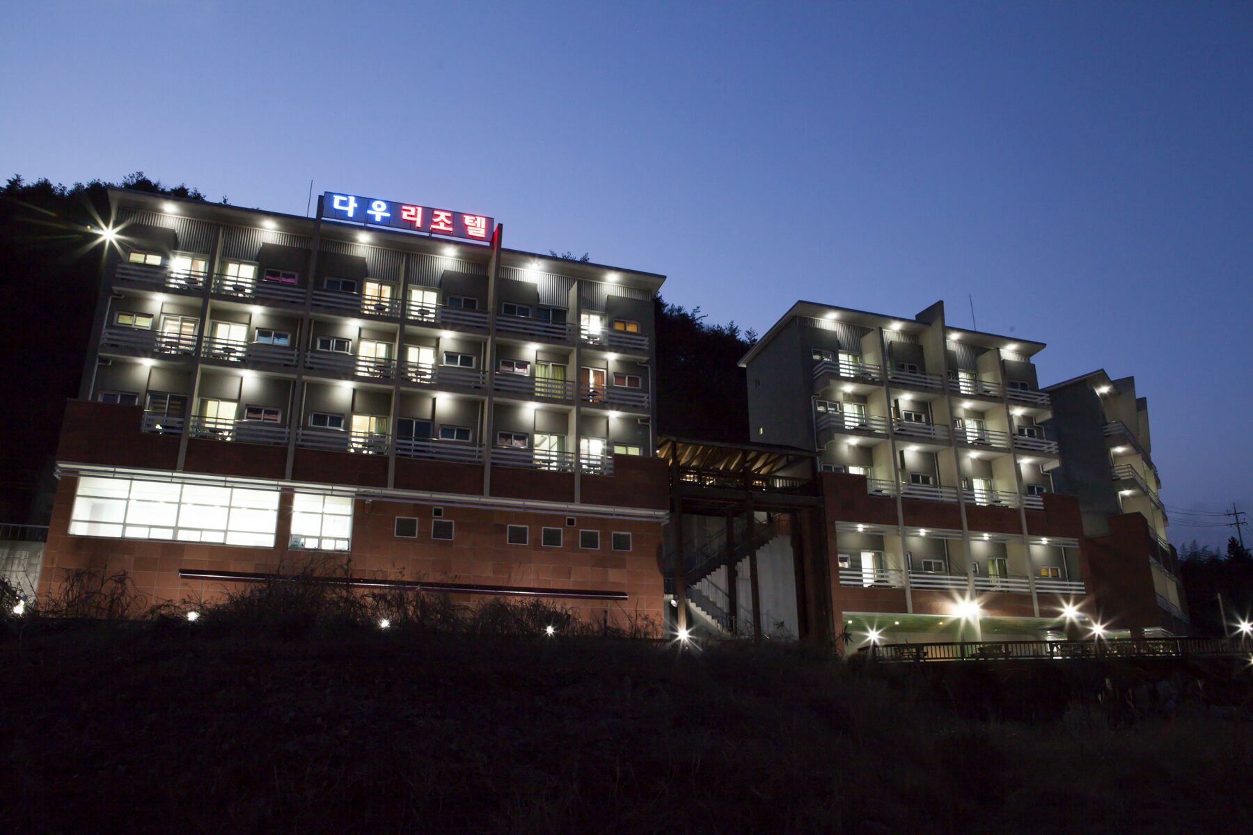 Un hotel de varios pisos con un letrero llamativo en un idioma extranjero, múltiples balcones y una fachada bien iluminada.