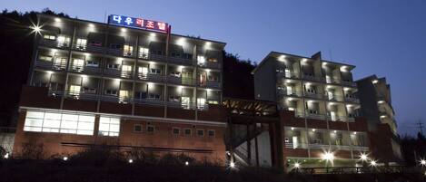 Un hotel de varios pisos con un letrero llamativo en un idioma extranjero, múltiples balcones y una fachada bien iluminada.