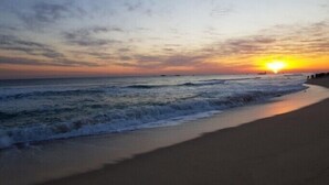 Une plage au coucher du soleil, avec des vagues et un ciel dégagé.