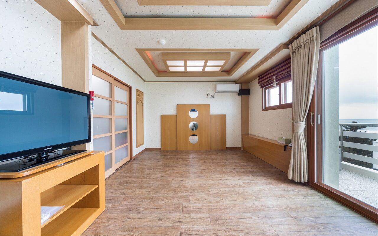 Una camera d'albergo con un'ampia televisione a schermo piatto su un supporto in legno, una porta scorrevole con cornice in legno, un soffitto con finestra a lucernario e un'ampia finestra con tende.