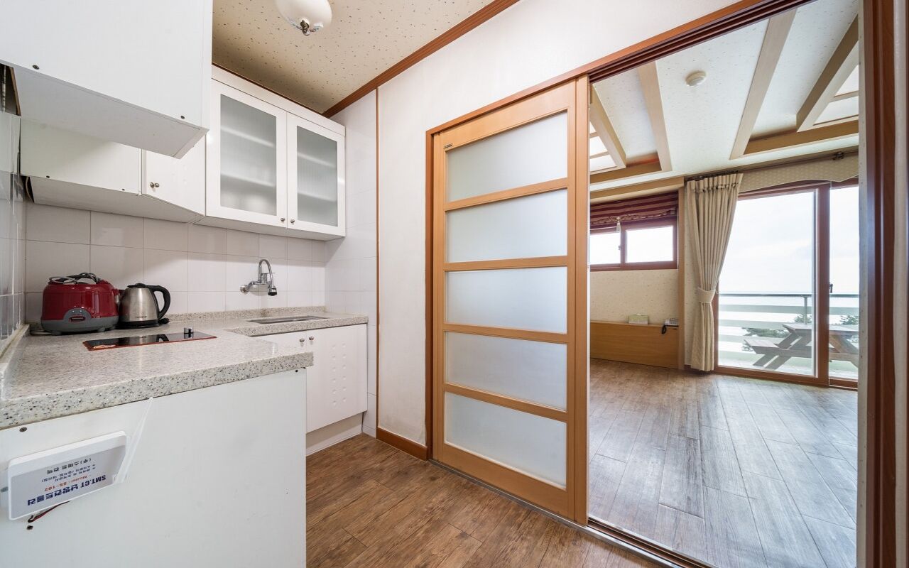 Una cocina con armarios blancos, un hervidor rojo y piso de madera.