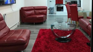 A modern living room with red leather sofas, a glass coffee table, and a red rug. A TV is mounted on the wall, and a kitchen is visible in the background. - Nice 2 Bed Independent Annex in High Wycombe (High Wycombe)