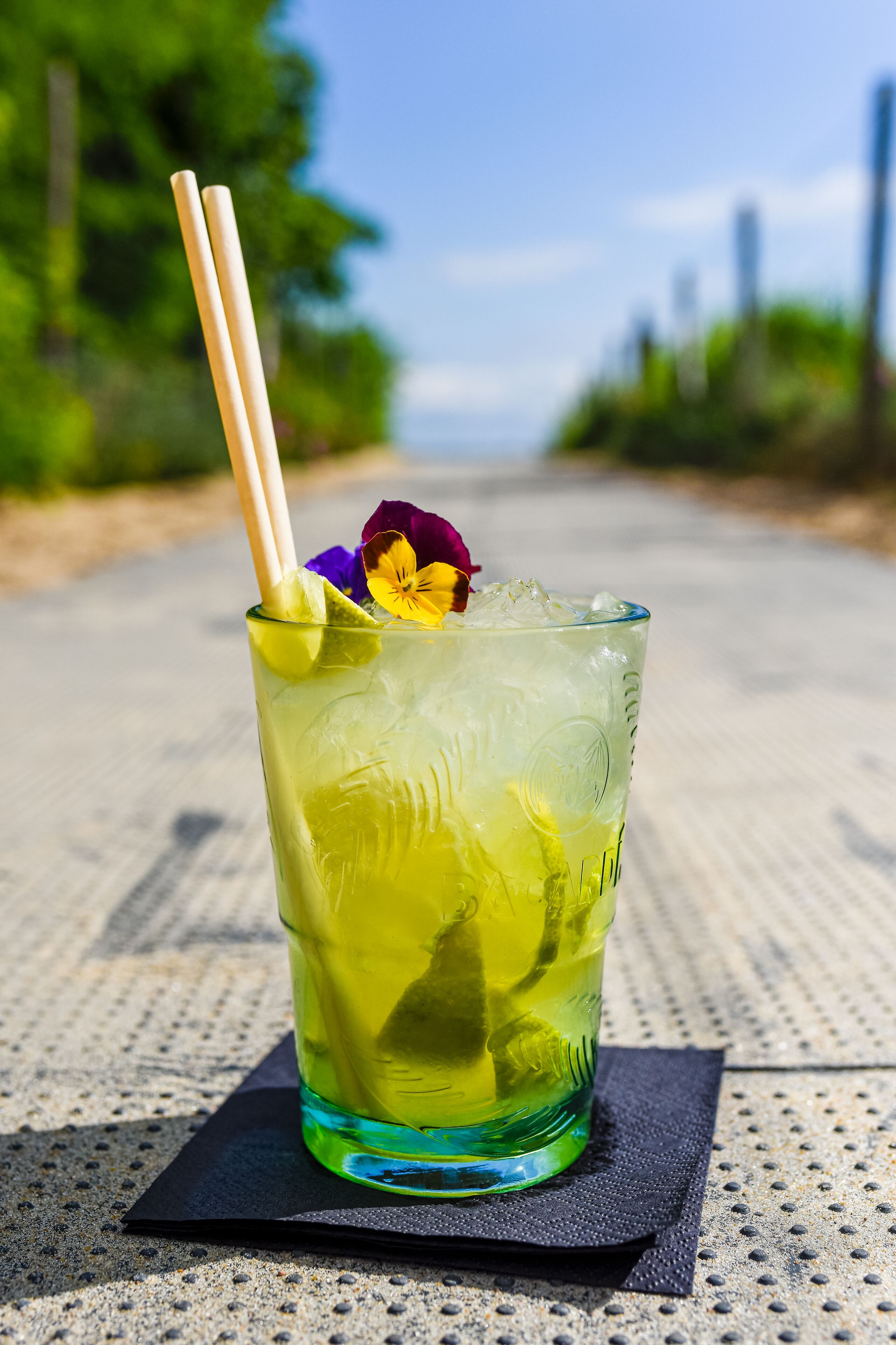 Ein Glas gelbes Getränk mit einer Blume und einem Strohhalm auf einer strukturierten Oberfläche.